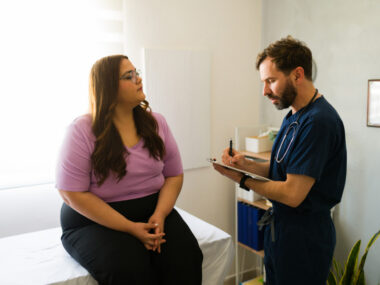 A medical professional takes notes on a clipboard while talking with a patient.