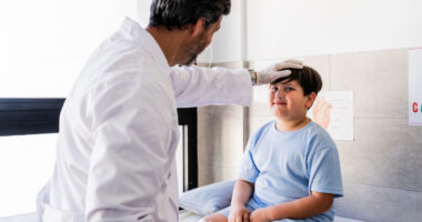 A doctor places his hand on a young patient's forehead during an examination.
