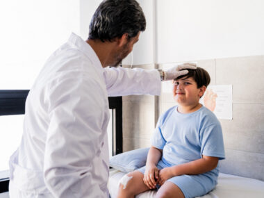 A doctor places his hand on a child's forehead during an examination.