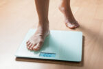 In a close-up image of a scale, a person is seen stepping on it, with one foot still on the floor.