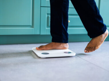 A photo shows the feet and lower legs of a person stepping on a scale.