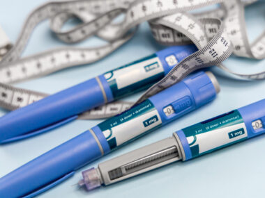 Three drug injection pens are seen alongside a long measuring tape.
