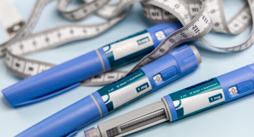 Three drug injection pens are seen alongside a long measuring tape.