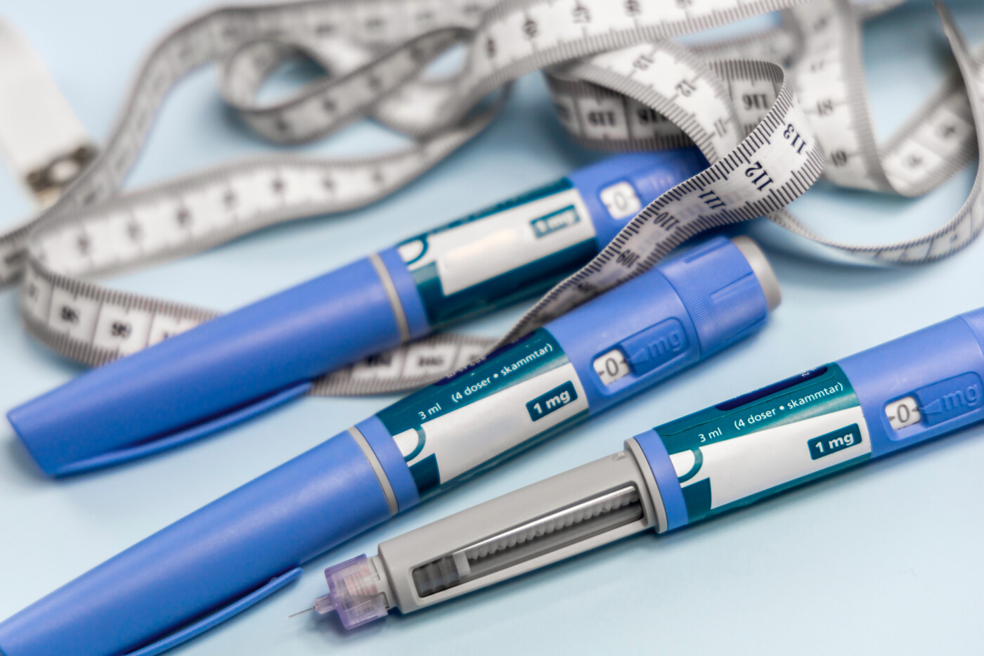 Three drug injection pens are seen alongside a long measuring tape.