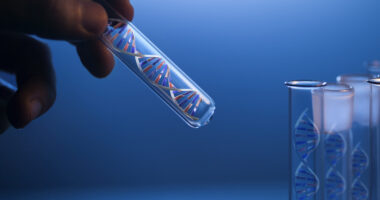 A hand holds a glass tube containing a DNA molecule next to several identical tubes.