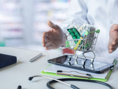 An image of medications in a miniature shopping cart on a tablet in front of a healthcare professional.